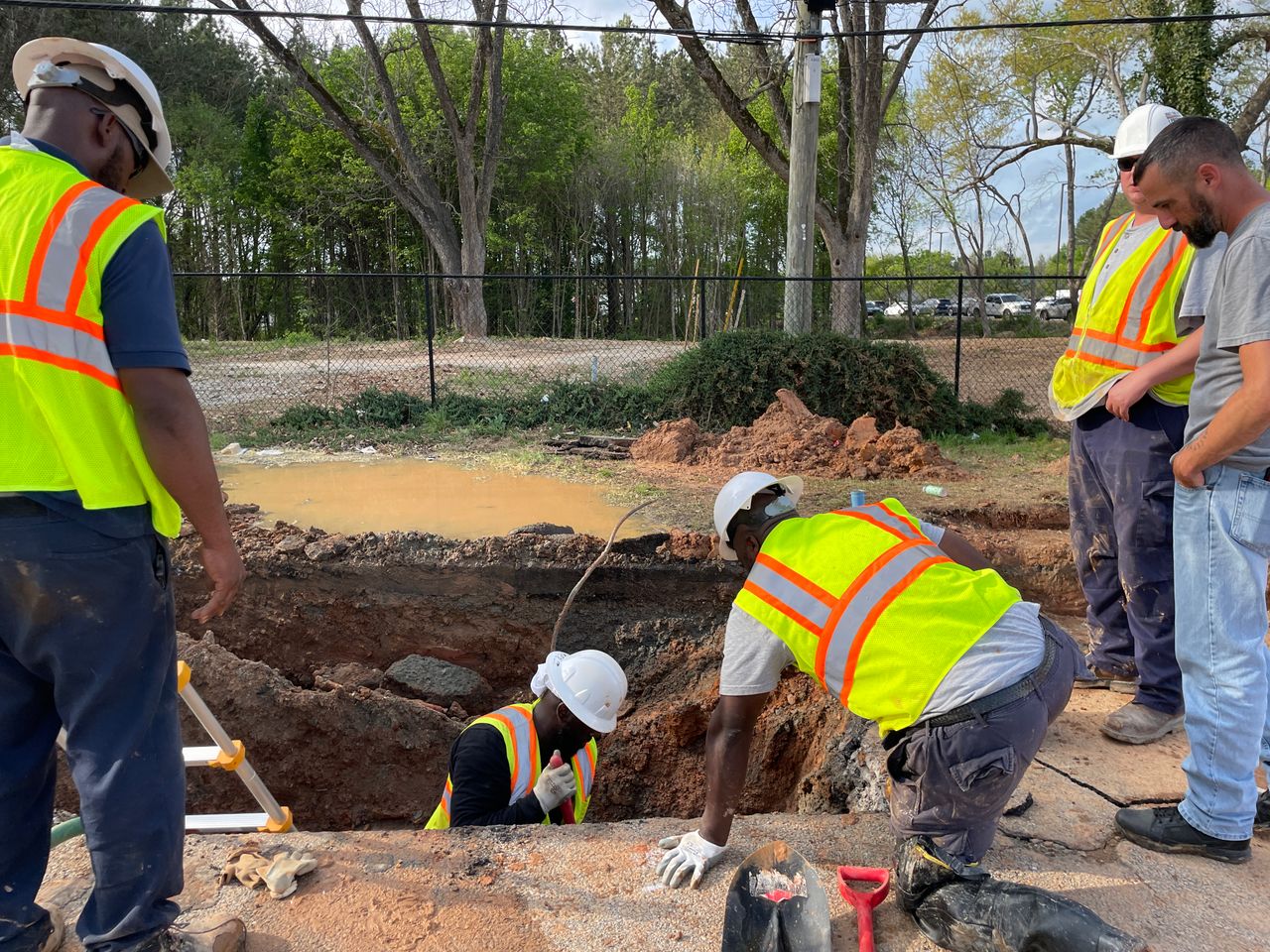 About Team of construction workers inspecting an underground utility site on a sunny day.