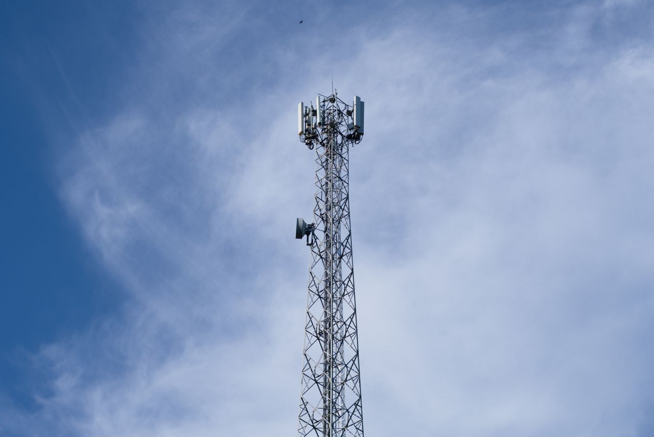The Art of Drawing Readers In: Your attractive post title goes here A tall metal communications tower stands against a backdrop of a clear blue sky with scattered clouds.